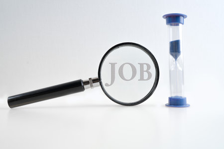 Magnifying glass and hourglass on a white background. Time to look for a job. Lettering JOB