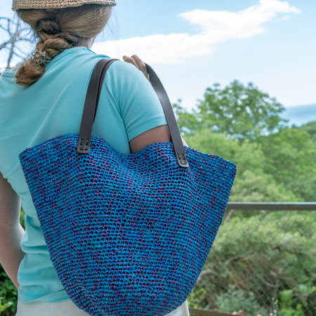 A woman holds a hand-crocheted bag against a backdrop of mountainsの写真素材