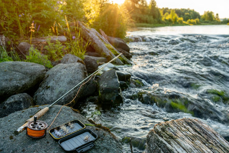 A fly fishing rod and an open fly fishing box lie on the rocks of a mountain river.の写真素材