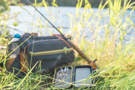 A fly fishing rod and an open fly fishing box lie on the rocks of a mountain river.