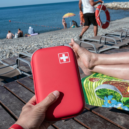 A red first aid kit with a white cross is among the necessary things for a holiday at sea. The concept of first aid in tourist travel.の写真素材