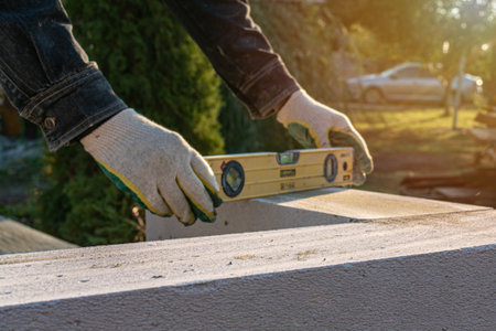 Mason using spirit level to check new autoclaved aerated concrete block wall outdoors. Wall...
