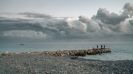 Men with fishing rods on the breakwater as the ship sets out to sea. Evening at sea.の写真素材