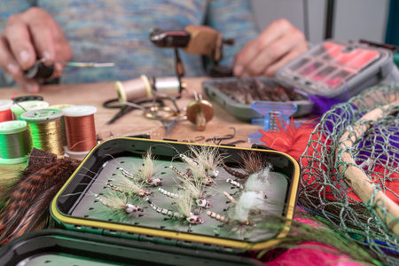 Man making trout flies. Fly tying equipment and material for fly fishing preparation.