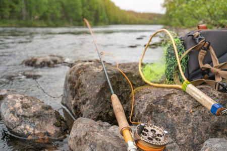 A fly fishing rod lies on the rocks of a mountain river against the backdrop of a sunset.