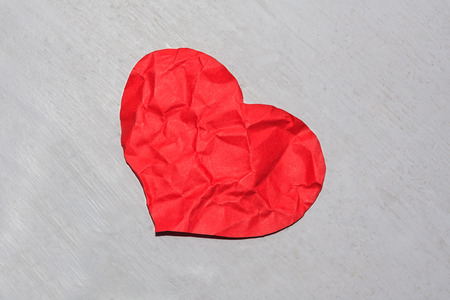 Abandoned crumpled red paper heart on a dirty shaded background