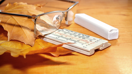 Glasses, ruler and chalk with yellow maple leaves on a wooden backgroundの写真素材