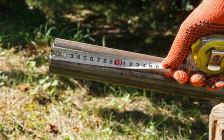 Two iron pipes and a gloved hand with a tape measure measuring the lengthの写真素材