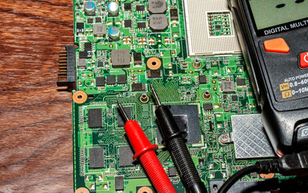A computer motherboard an digital multimeter and a red and black dipstick of one tool on it. The...