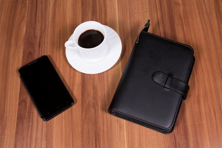 Cup of coffee,phone and notebook on wooden backgroundの写真素材