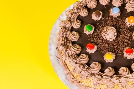 Tasty chocolate and hazelnut birthday cake colorful candy adorned on yellow backgroundの写真素材