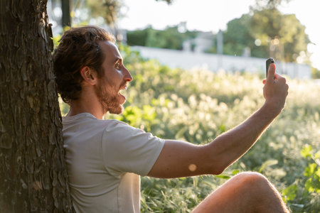 Man making a video call in a park on a sunny afternoonの写真素材