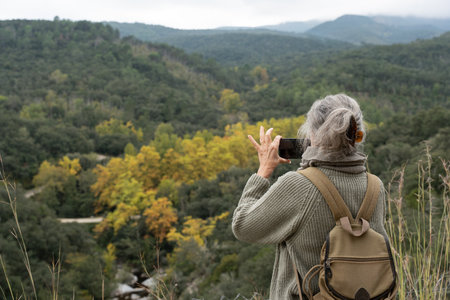 Senior woman hiking mountains taking pictures with smartphoneの写真素材