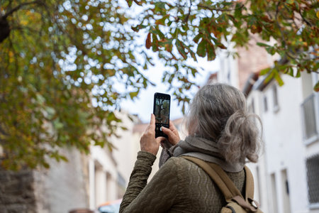 Senior woman taking picture with smartphone in the street enjoying retirementの写真素材