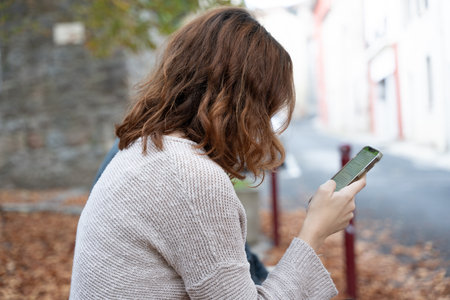 Woman texting on phone or scrolling on social networks in urban autumn streetの写真素材