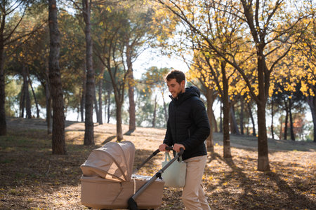 Young father walking baby stroller in autumn urban park in a sunny day