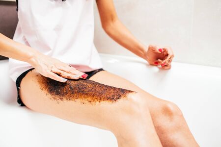 Slim young woman in a bright silk pajamas scrabs her leg sitting in a big beautiful bright bath. Skin care conceptの写真素材