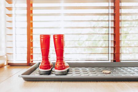 Kids Red rubber shoes in the hall of the house. Bright red gardening boots. Garden Rainy Shoes. Autumn,spring kids boots conceptの写真素材