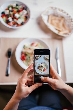 Close up hands of woman taking photo of fresh salad on the table with her phone. Social media concept.の写真素材