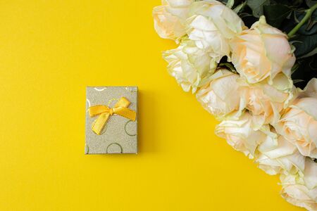 Gift box and white roses on yellow background from above, flat lay frame