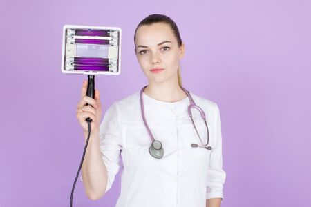 Medical concept of young beautiful female doctor in white coat with stethoscope. Woman hospital worker looking at camera, blue background.の写真素材