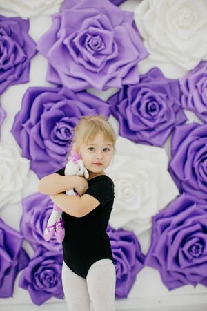 beautiful young blonde girl engaged in gymnastics on a white and purple roses background in a black suitの写真素材