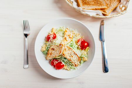 Fresh healthy caesar salad with chicken on white wooden table with fork and knife. Top view....