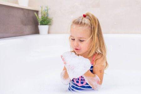 Little blonde girl taking bubble bath in beautiful bathroom.Kids hygiene. Shampoo, hair treatment and soap for children. Kid bathing in large tubの写真素材
