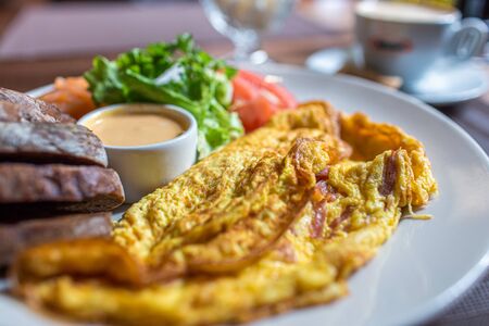 Fresh omelette served with green salad, tomatoes. sause and breab - close up view. Cup of coffee on a background. Traditional breakfast. Healthy food in cafeの写真素材