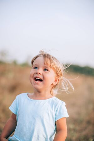 Close up portrait of little blonde girl with blue eyes outside with tousled hair and smiling face. Childhood in the countryの写真素材