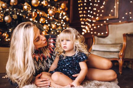 Mother and daughter in shiny clothes hugging and smiling, winter evening together at home in a decorated living room at Christmas Eve.の写真素材