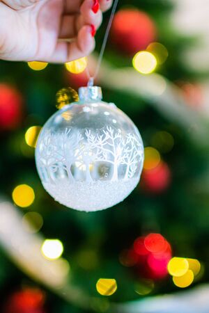 Christmas, decoration, holidays and people concept - close up of woman hand holding christmas ball over living room and tree backgroundの写真素材