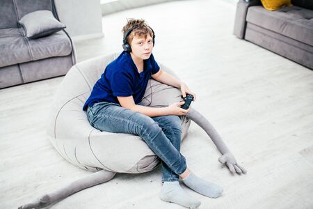 Gaming video games concept - teenage boy playing game with joystick and headphones, enjoying sitting...