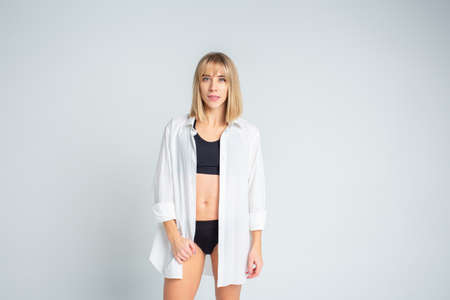 Beautiful slim blonde woman posing in black lingerie and wearing a white mens shirt on a white background. Copyspaceの写真素材