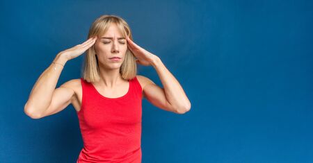 Young woman wearing red shirt standing over blue background with hand on head because indigestion, painful illness feeling unwell. Ache concept, migraineの写真素材
