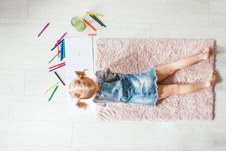 Top view of charming little girl drawing using colorful pencils while lying on the floor in her room at home.の写真素材