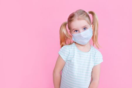 Little blonde girl with two ponytales in a medical mask face on a pink background looking at the camera.の写真素材
