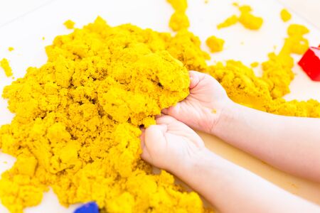 Yellow magic sand in a kids hands on a white background close up. Early sensory education. Preparing for School. Development.の写真素材