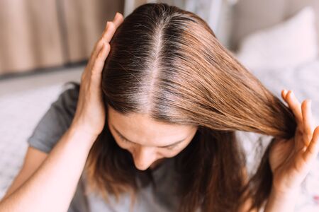 Closeup of a woman's head with parted gray hair regrown roots becouse of quarantine.