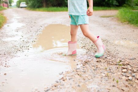 Little girl in blue wear jumping into a puddle in the village. Summer vacation, holidays, childhood....