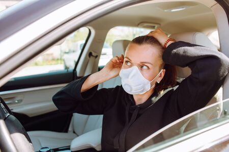 Woman with protective mask at her face and sitting in the car and brush her hair. Quarantine concept.の写真素材