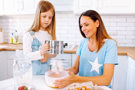 An attractive smiling family of mother daughter baking in a light kitchen at homeの写真素材