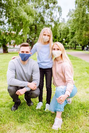 Family members embracing each other, smiling in the camera wearing cloth face masks. Father, mother and daughter protect themselves from the virusの写真素材