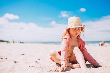 Adorable toddler girl in hat playing on white sand beach at the beach. Summer, vacationの写真素材