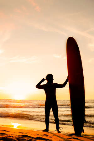 Male surfer silhouette with yellow longboard on a ocean coast at sunset. Water sport adventure camp and extreme swim on summer vacationの写真素材