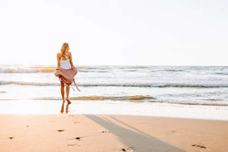 A young slim girl stands walking on the beach or ocean and look at the horizont. A woman dressed in a warm sweater. Tonedの写真素材