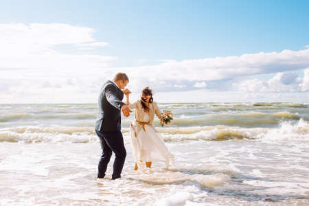 Happy bride and groom on the beach sea having fun. Newlyweds couple jump into sea water waves at sunny summer day. Just married.の写真素材