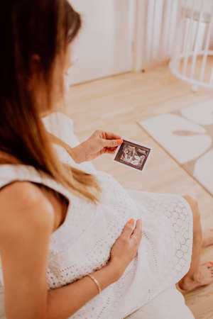 Pregnant woman looking at her baby twins sonography. Happy expectant mother enjoying first photo of...
