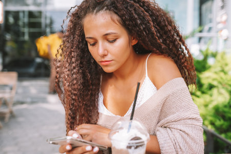 Young woman addicted to technology. Female use smartphone sitting at cafe and drinking beverage.の写真素材