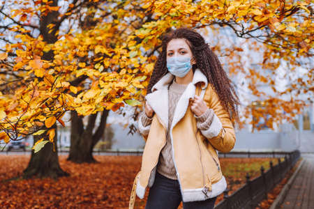 Beautiful afro haired woman wearing protective medical face mask stand on the street of city. Female...